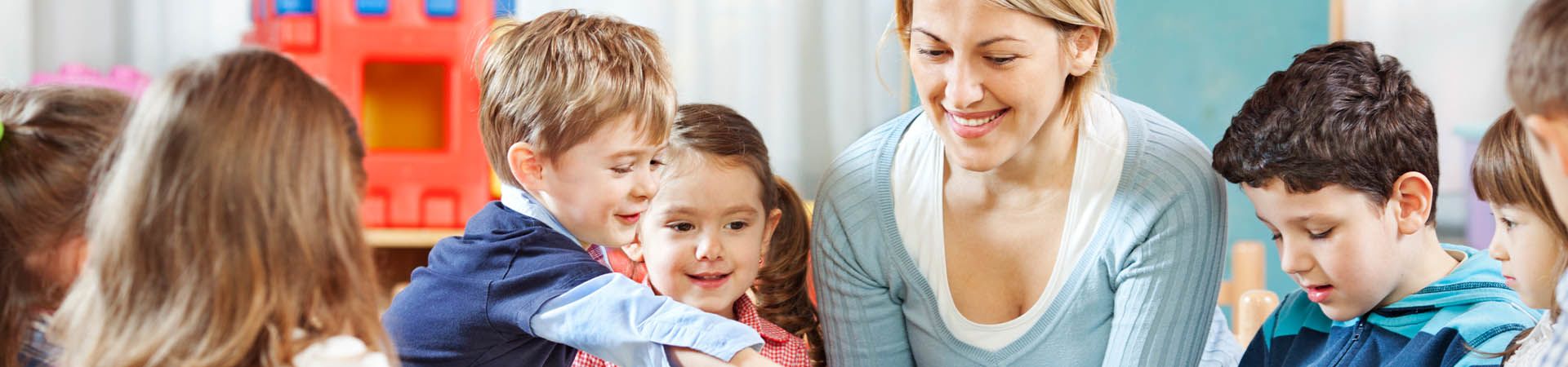 Lesespiele: Kinder sitzen mit einer Betreuerin am Tisch und lernen spielend Lesen.