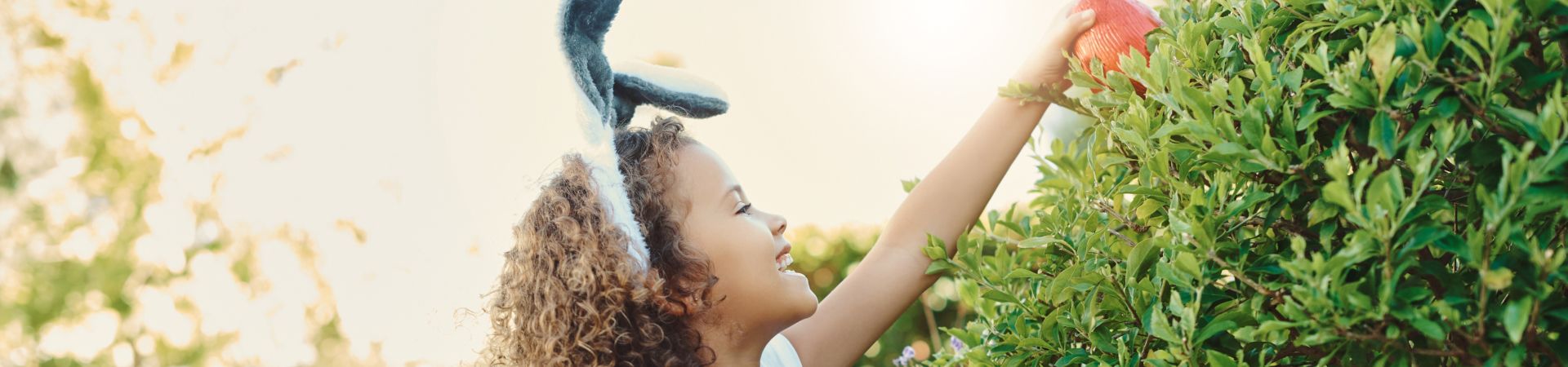 Easter gifts for children: a young girl collecting Easter eggs in a garden.