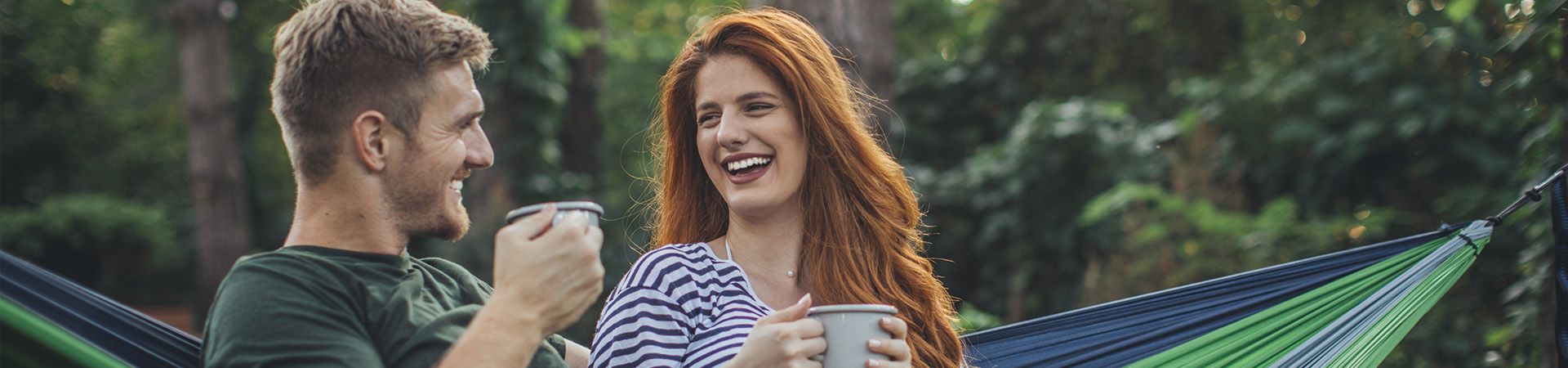 Plastic-free travel: holidaymakers relaxing in a hammock and drinking out of enamel mugs.