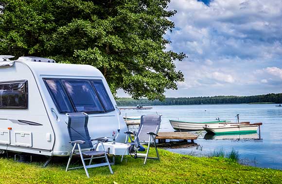 Campingregels: caravan staat met campingmeubels aan een meer. Campingregels: caravan staat met campingmeubels aan een meer.