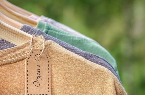 Ubrania z ekologicznej bawełny wiszą na drewnianym wieszaku.