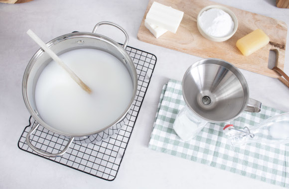 Make your own homemade liquid laundry detergent: using a funnel to fill a bottle with the cooled detergent.