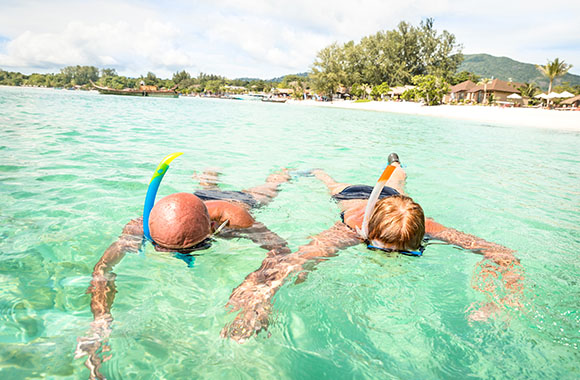 Un homme et une femme font du snorkeling dans une eau turquoise.