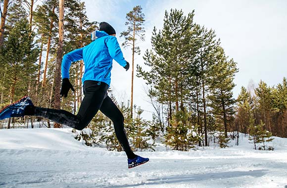 Bieganie w zimie – mężczyzna biegnie po pokrytej śniegiem ścieżce.