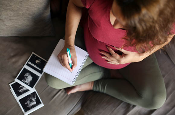 Una mujer embarazada escribe en una libreta una lista de nombres para niños. Una mujer embarazada escribe en una libreta una lista de nombres para niños.