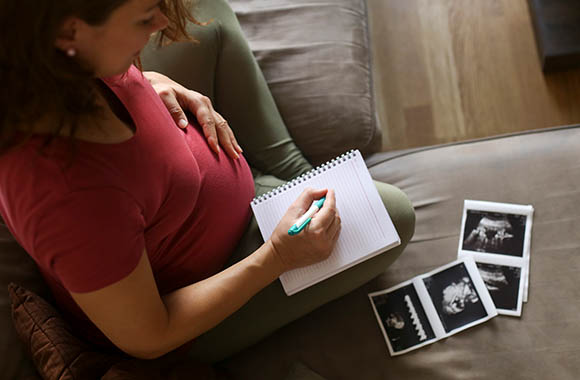 Schwangere Frau schreibt eine Liste mit möglichen Babynamen.