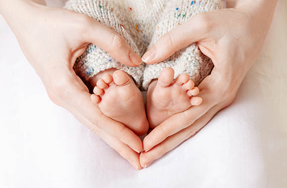 Le mani di una mamma formano un cuore mentre stringe i piedini del suo bambino. Le mani di una mamma formano un cuore mentre stringe i piedini del suo bambino.
