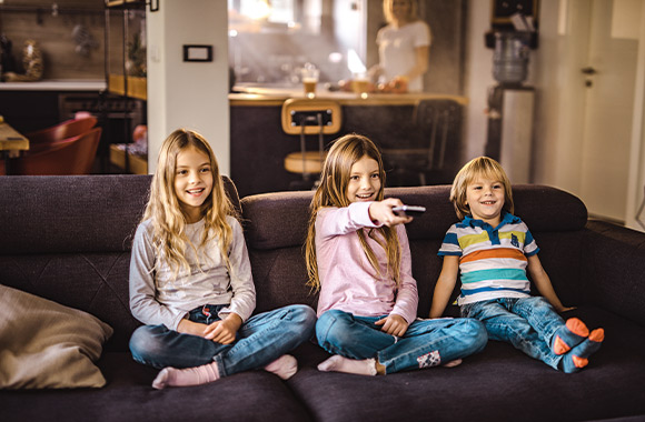 Streaming kinderen - twee zusjes en broertje kijken samen tv op de bank.