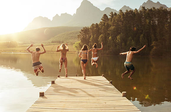 Grupa młodych ludzi skacze z pomostu do górskiego jeziora