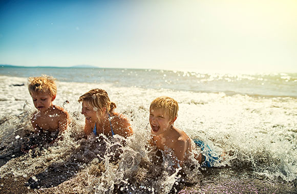 Twee blonde jongetjes liggen met hun moeder in de zee.