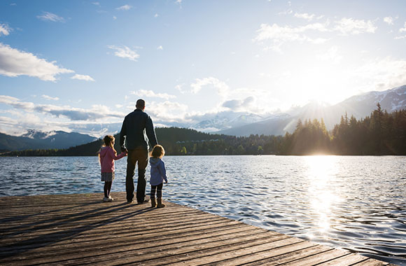 Zwei kleine Mädchen mit Vater am Steg schauen auf Bergsee
