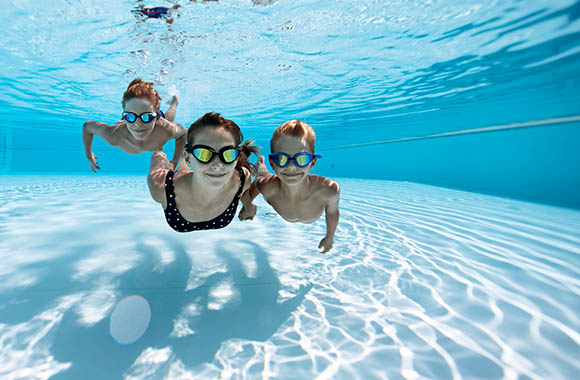 Three children with swimming goggles diving in the pool. 