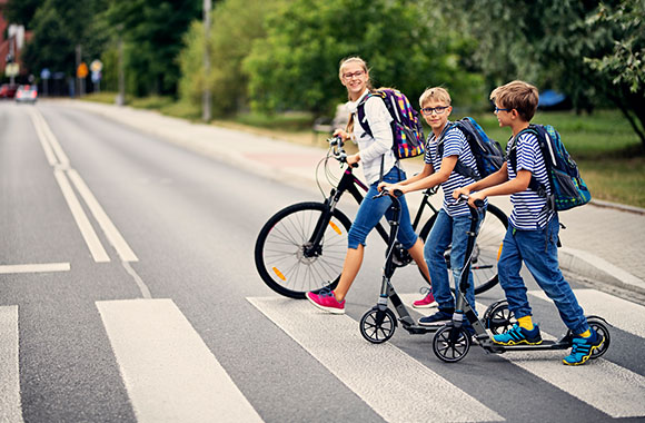 DRowerem do szkoły – Grupa dzieci jadąca do szkoły na rowerze i hulajnogach