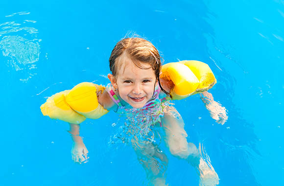 Dziewczynka w rękawkach do pływania uczy się utrzymywać na wodzie w brodziku.