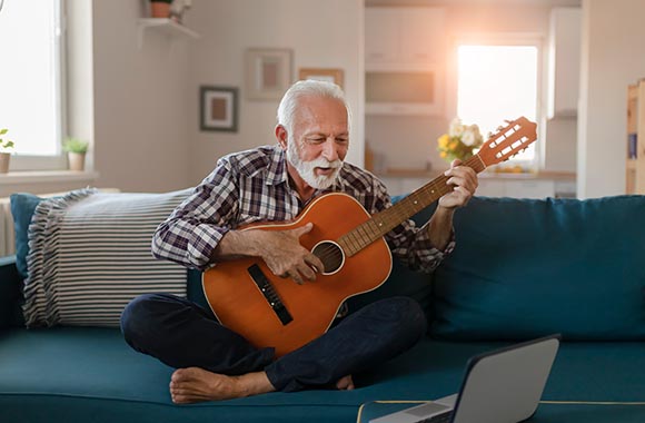 Loisirs en ligne : un sénior apprend à jour de la guitare avec une vidéo en ligne.