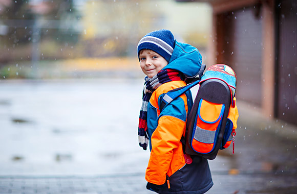 Kleine jongen in reflecterende jas en met reflectoren op de schooltas op weg naar school Kleine jongen in reflecterende jas en met reflectoren op de schooltas op weg naar school