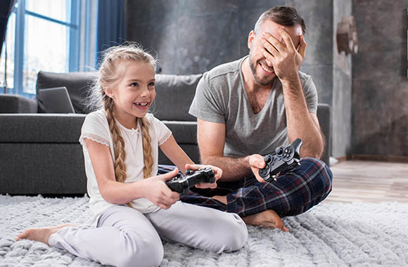 Un père et sa fille devant un écran en train de jouer à un jeu vidéo