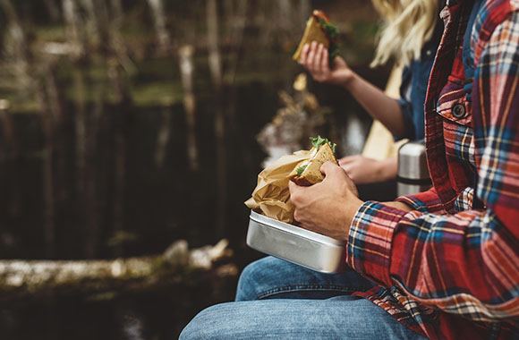 A group of hikers eating the provisions they brought with them from metal lunch boxes.