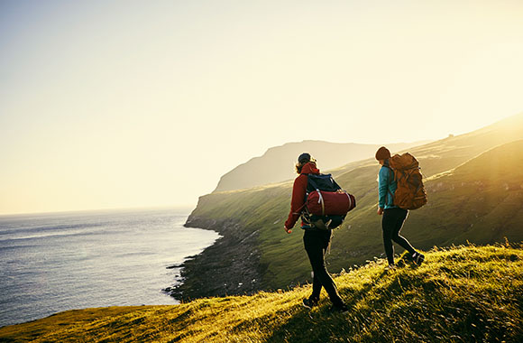 Two hikers with full hiking gear approach the coast.