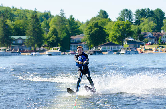  Wasserski fahren – Frau im Neoprenanzug fährt hinter einem Motorboot Wasserski.