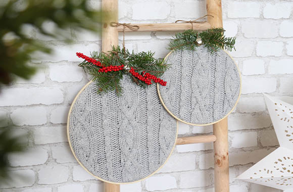 Upcycling Kerstmis knutsel idee: borduurraam bedekt met een oude gebreide sjaal met een vlechtpatroon.