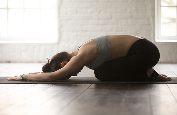 Woman in Balasana yoga pose kneeling on a yoga mat.