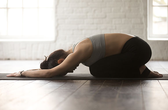 Woman in Balasana yoga pose kneeling on a yoga mat. Woman in Balasana yoga pose kneeling on a yoga mat.