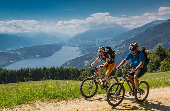 Cómo preparar un viaje en bici: dos ciclistas en ruta con las vistas de un lago de fondo.