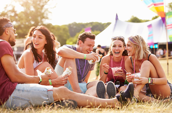 Festival guide: friends sitting and eating together on a field at a festival. Festival guide: friends sitting and eating together on a field at a festival.