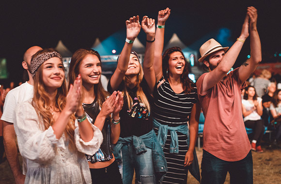 Festivalgoers in stylish festival looks and cheers on a band. Festivalgoers in stylish festival looks and cheers on a band.