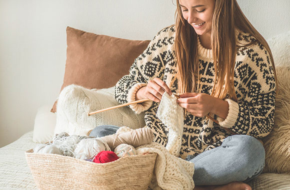 Learning to knit: A woman knits a white scarf.