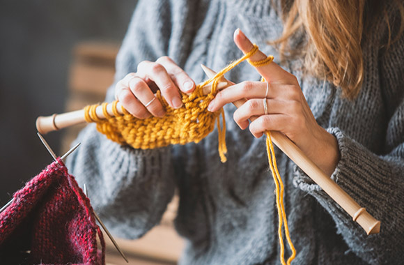 Learning to knit: A woman knits with yellow wool.