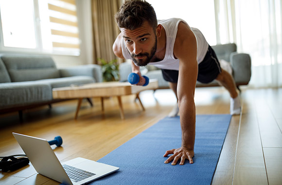 Workout for at home – man training with dumbbells at home in front of a laptop.
