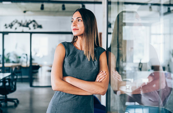 Une femme d'affaires en tenue moderne est adossée à un mur de verre.