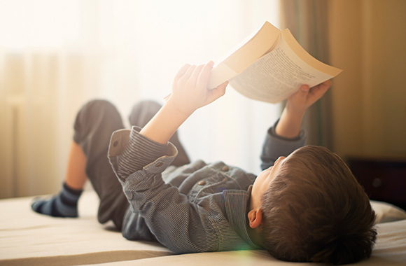 Jongen ligt op bed en leest een boek. Jongen ligt op bed en leest een boek.
