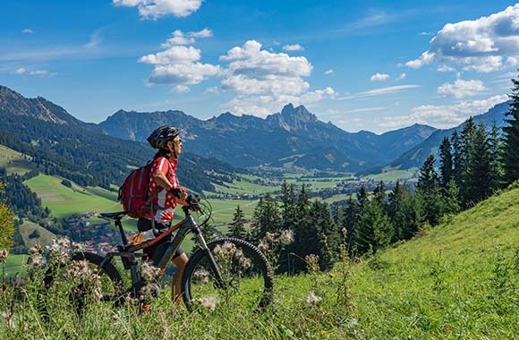 Radtouren Tirol: Eine Frau steht mit einem Fahrrad auf einer Wiese in Tirol.
