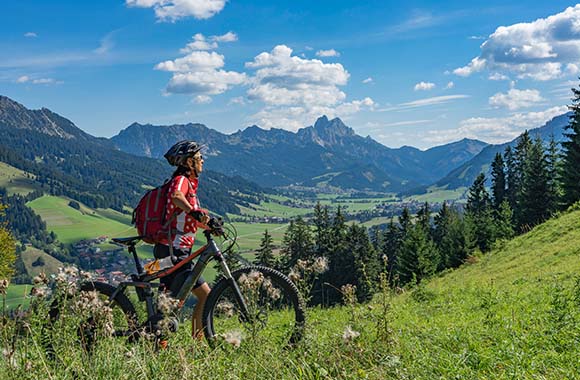 Radtouren Tirol: Eine Frau steht mit einem Fahrrad auf einer Wiese in Tirol. Radtouren Tirol: Eine Frau steht mit einem Fahrrad auf einer Wiese in Tirol.