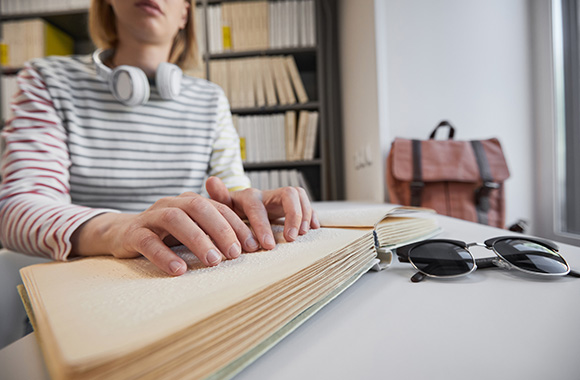 Studia dla niepełnosprawnych: niewidoma studentka czyta notatki wydrukowane brajlem. Studia dla niepełnosprawnych: niewidoma studentka czyta notatki wydrukowane brajlem.