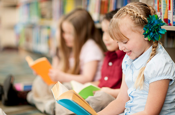 Lesen lernen: Mädchen liest mit Freunden in der Bibliothek. Lesen lernen: Mädchen liest mit Freunden in der Bibliothek.