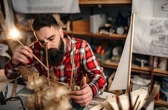 Kreatywne hobby dla dorosłych: mężczyzna składa model statku z drewna.