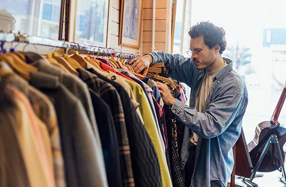 Duurzaamheid - Man is op zoek naar een jas in een tweedehandswinkel.