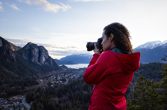 Learning to take photos: A woman taking a photo of a mountain landscape.