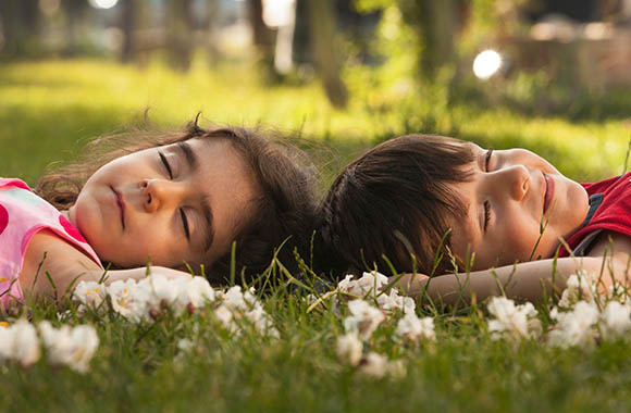 Twee kinderen liggen met gesloten ogen op een weide en luisteren naar de geluiden van de natuur. Twee kinderen liggen met gesloten ogen op een weide en luisteren naar de geluiden van de natuur.