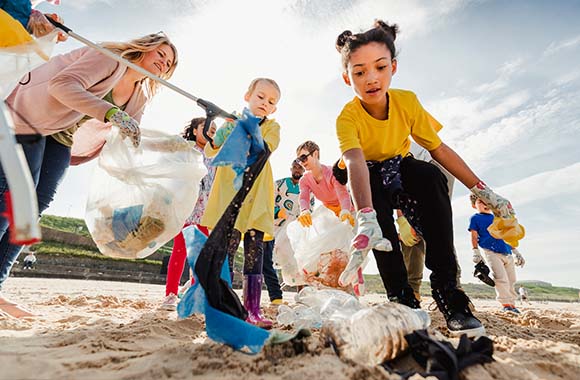 Tkaniny z recyklingu: grupa dzieci i dorosłych zbiera na plaży plastikowe śmieci do recyklingu.