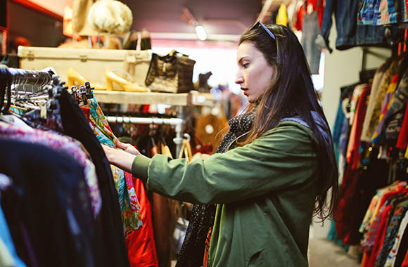 Vrouw doorzoekt kledingrekken in kringloopwinkel.