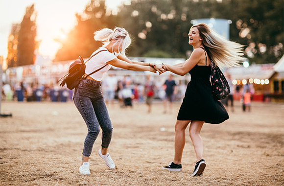 Sporty outfits for festivals: friends dancing together on a field at a festival.