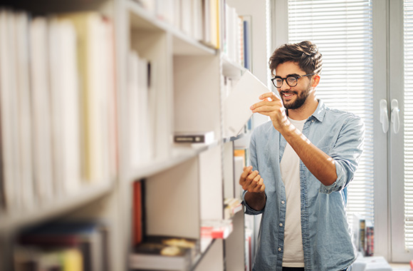 Man zoekt in de bibliotheek naar een boek voor persoonlijke ontwikkeling.