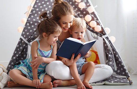 Leseförderung im frühen Kindesalter: Mutter liest mit ihren beiden Kindern in einem Buch.