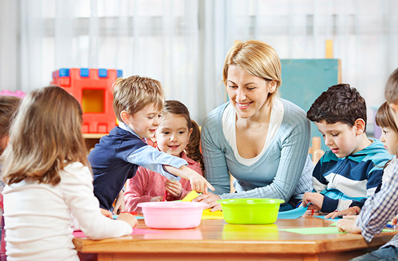 Lesespiele: Kinder sitzen mit einer Betreuerin am Tisch und lernen spielend Lesen.