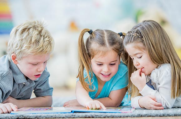 In der Vorschule Lesen lernen: Kleinkinder schauen ein Bilderbuch an.